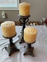 Front view of three bronze-colored candle holders with cream swirl candles