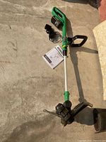 Full view of grass trimmer with charger, adapter and manual on floor