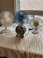 All four electric desk fans on table showing size and color differences
