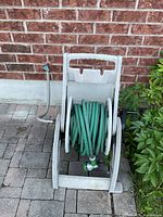 Front view of hose reel with hose and nozzle against brick wall