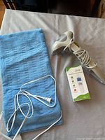 Heating pad, handheld massager with wrapped cord, and boxed Breo device laid on surface