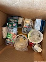 Overview of box containing assorted screws, electrical outlets/switches, utility string, lubricant can, plastic anchors and containers