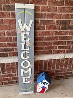 Full view of welcome sign and birdhouse together against brick wall