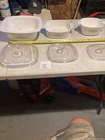 Overall view of three Corning Ware casseroles with lids and tape measure for size reference