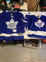 Both Toronto Maple Leafs jerseys hung on hangers on table