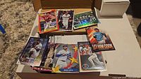 Open cardboard storage box filled with several hundred Topps baseball cards; sample cards displayed on top show various designs including coloured parallels, rookies and veterans