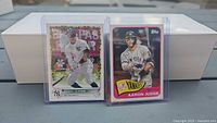 Two Aaron Judge Topps baseball cards in plastic toploaders with white storage box behind