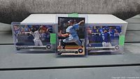 Front view of three Topps Now Blue Jays rookie cards in top-loaders with storage box behind