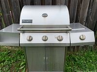 Front view of Charmglow stainless steel propane grill with lid closed and sided shelves visible