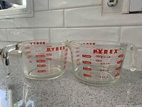Two Pyrex glass measuring cups side by side showing handles and red graduations.