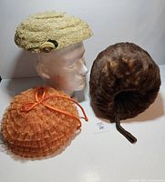 Three items: cream lace hat on mannequin, brown fur muff, orange mesh hat