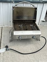 Front view of Nexgrill portable propane grill with lid open showing cooking grate, knobs, hose and regulator