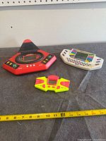 All three handheld electronic games on table with measuring tape for scale