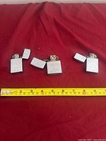 Three open Zippo lighters on red cloth with tape measure for scale