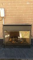 Front view of black metal electric fireplace insert showing glass panel, faux logs and overall exterior