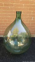 Full view of green glass demijohn bottle against brick wall