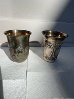 Front view of both sterling Kiddush cups showing differing ornate designs and tarnish