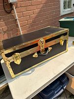 Full view of black steamer trunk with brass-tone hardware on table