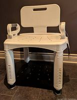Front view of adjustable shower chair showing seat with perforations, backrest, side handles and leg height markings