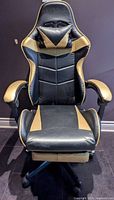Front view showing black and gold faux leather gaming chair, head pillow, padded arms, five-star base