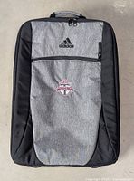 Front view of Adidas grey and black rolling carry-on suitcase with Toronto FC crest and Adidas logo