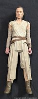 Front view of full 11-inch Rey action figure in desert outfit on black background