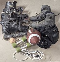 All items laid out: two pairs inline skates, football, baseball, skateboard truck with wheels, protective pads, skipping rope