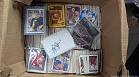 Open box showing assorted sleeved cards, top-loader cards, autograph sheet and CD case atop bulk cards