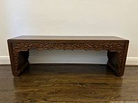 Full front view of carved wood bench showing ornate front apron and overall shape