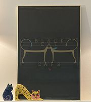 Full view of framed Black Cat Café poster with two wooden cats in front
