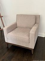 Front angled view of beige upholstered armchair on wood floor