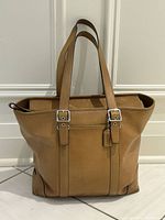 front view of tan leather Coach tote with hangtag and buckled straps