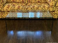 Front view of clear bent-glass coffee table against floral sofa background