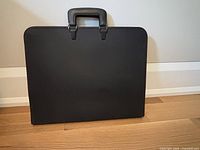 Front view of closed black portfolio case showing handles and textured exterior