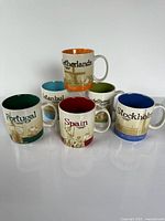 Front view of all six Starbucks city mugs displaying city names and colored interiors