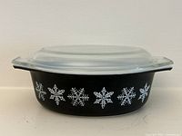 Side view showing black dish, white snowflake pattern, clear lid