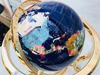 Close-up detail of the globe showing blue lapis stone, multi-colored inlays of continents, and gold grid lines with country names.