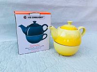 Yellow Le Creuset Tea for One pot and cup set with original box beside it on a cloth surface.