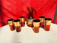 Full view of the ruby glass lemonade set with one pitcher and six glasses, all decorated with gold bands and floral enamel designs, set against a red background.