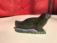 Side angle of dark green soapstone seal carving on white surface with red background.