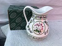 Front and side view of the white ceramic pitcher decorated with botanical floral patterns sitting atop green Portmeirion branded box, showing detailed flower wreaths and leaf garlands