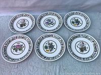 Full view of six vintage Portmeirion Variations dinner plates laid out on a cloth surface. Each plate features a distinct flower with butterfly in the center and floral decorative border rim.