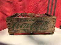 Front view of wooden Coca-Cola crate showing faded green logo and inside bottles with red caps.