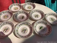 Set of ten Portmeirion bowls showing the floral designs and garland borders from a top angle on a white table with a red backdrop.