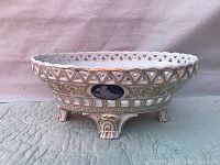 Side view of vintage fancy porcelain console bowl showing open lattice work rim, gold and blue classical decorations, and three ornate pedestal feet.