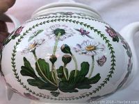 Close-up of the floral and insect detailed pattern on the teapot body highlighting daisies and butterflies.