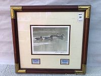 Framed Robert Bateman print showing four ducks on water with two stamps below, the frame is brown wood with brass corner accents.