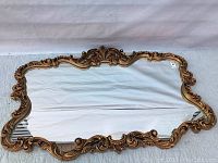 Full view of the mirror showing the ornate gold leaf and scroll carved frame in horizontal layout on a quilted background.