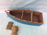 Horizontal view of vintage canoe shaped wooden bookcase showing three compartments, alongside two miniature wooden lobster traps on a quilted cloth surface.