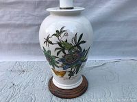 Front view of ceramic lamp showing botanical and butterfly designs, including Passiflora Caerulea Blue Passion Flower and yellow butterfly, on white glossy surface with wooden base.